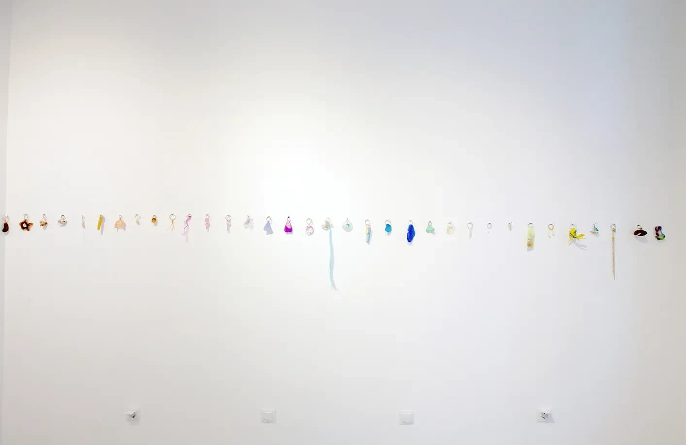 A long row of small hanging trinkets and charms along the gallery wall