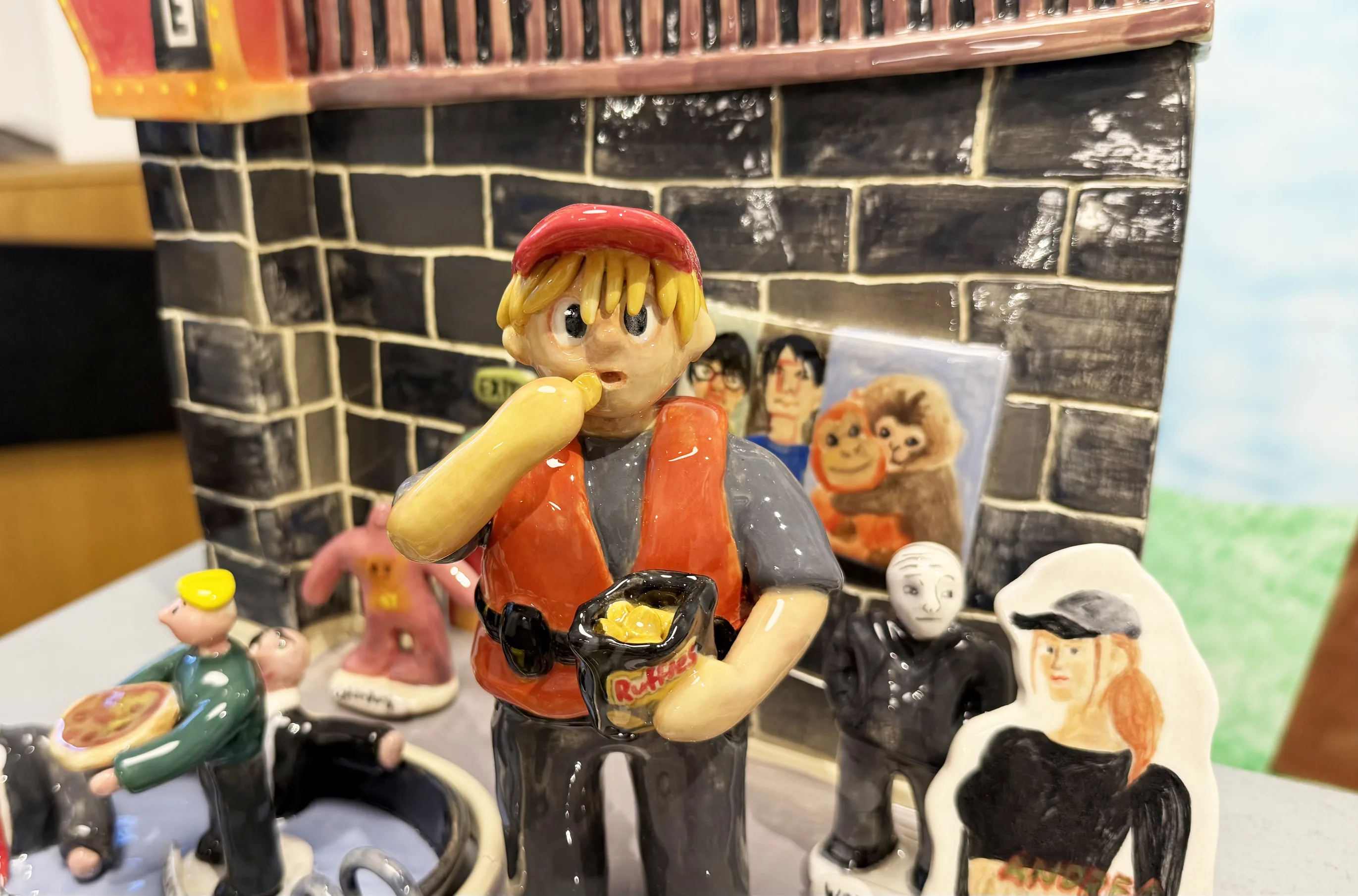 Detail of The Palace: glazed figures in front of the brick store, one in a red cap eating noodles