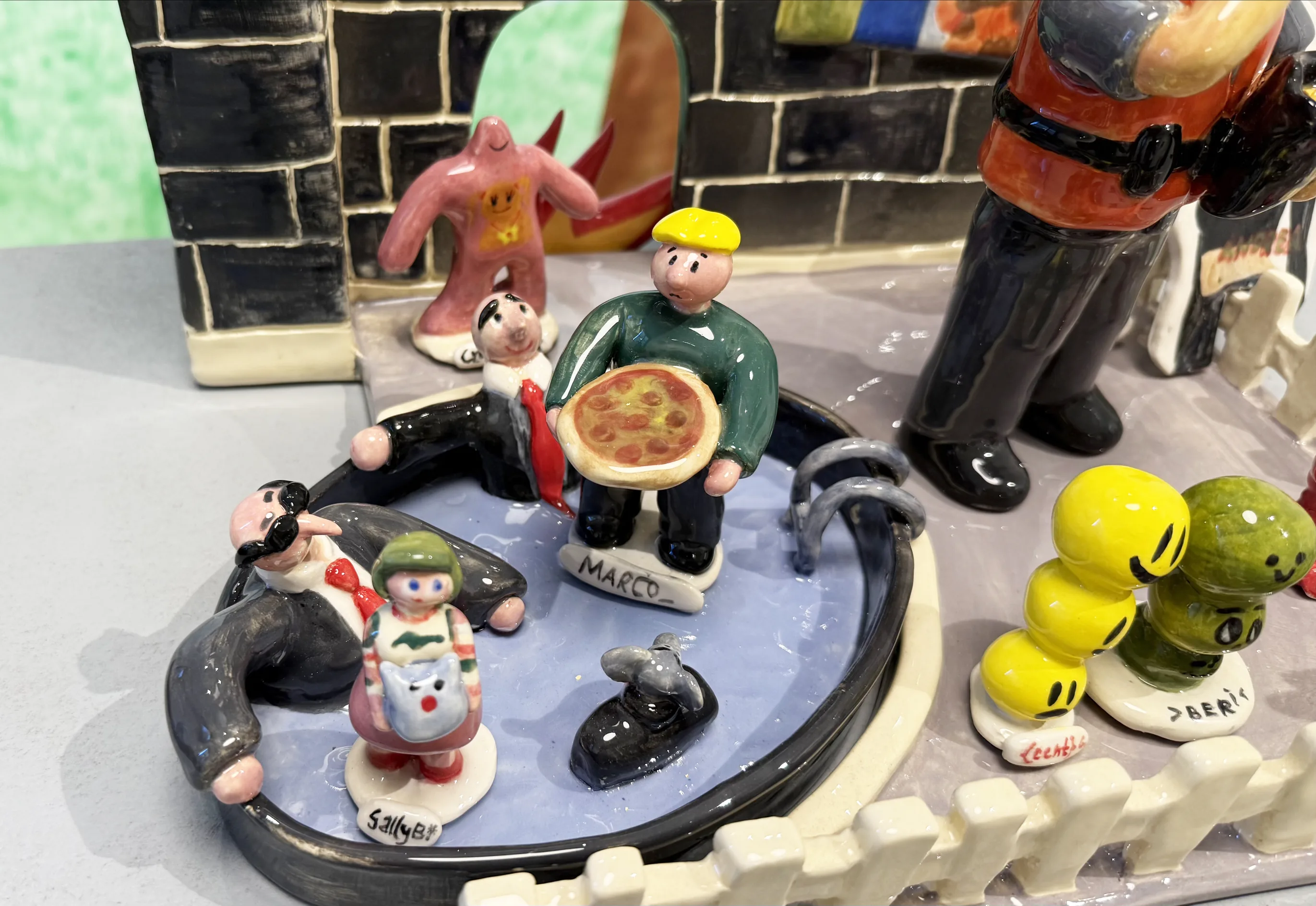 Detail of The Palace: small glazed figures around a pool, one holding a pizza