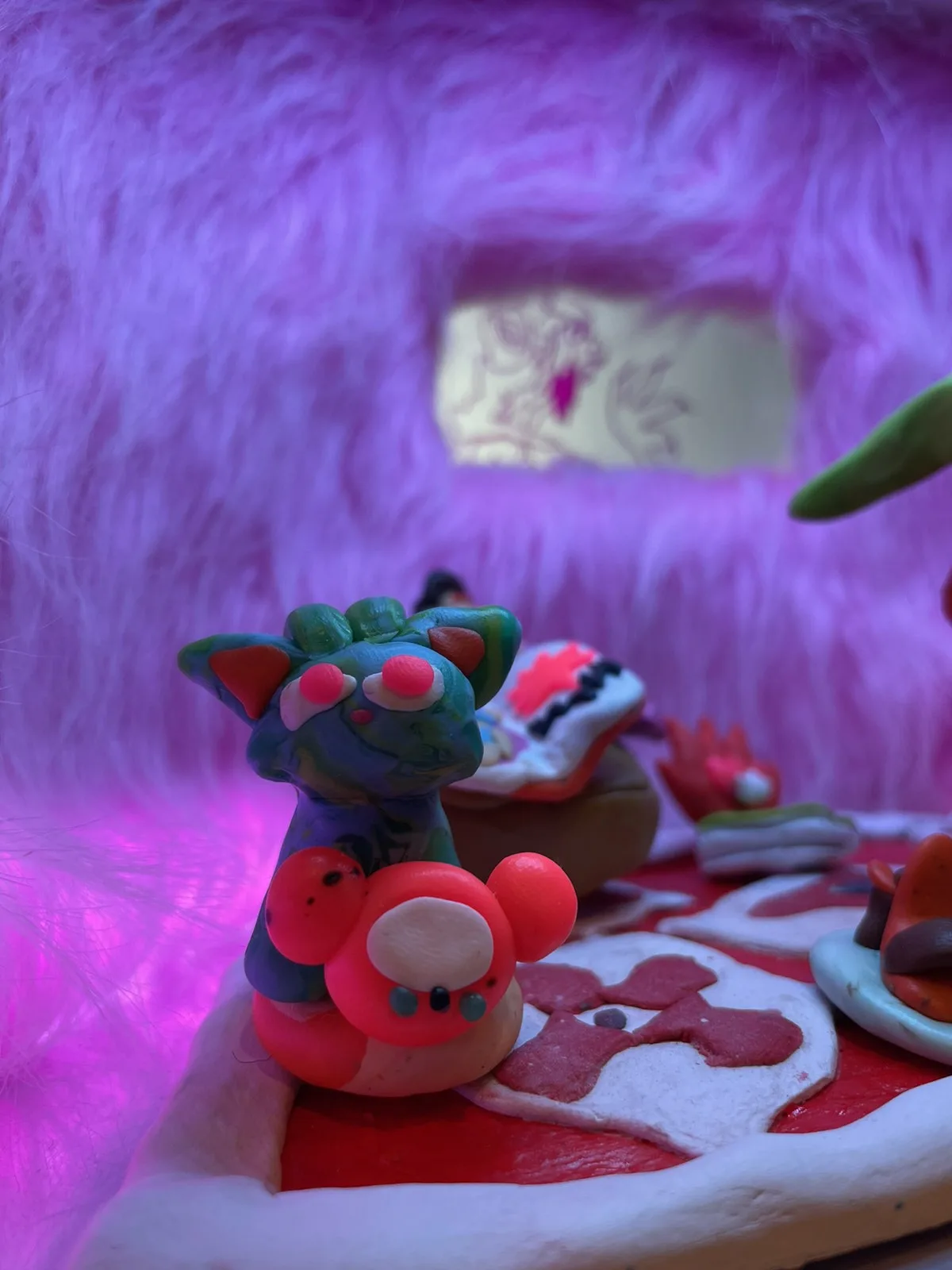 Close-up of a clay cat-like figure with red eyes in front of the window, under purple light