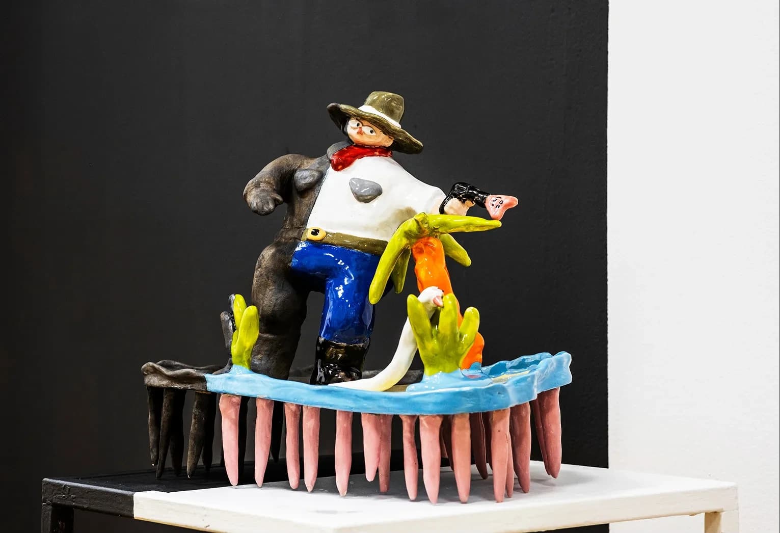Ceramic sculpture of a cowboy figure with a pistol, seated above a row of pink comb-like teeth