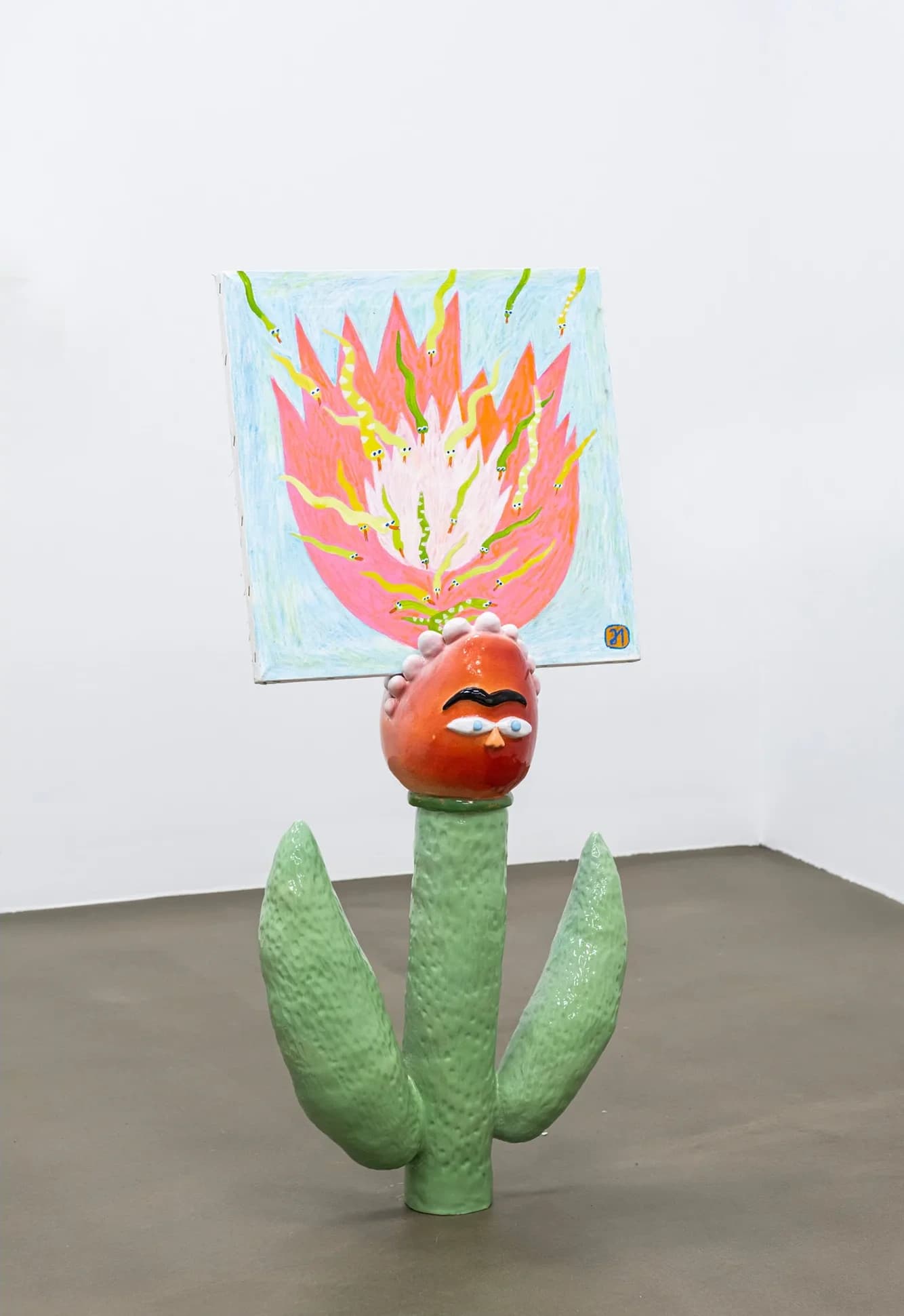 Ceramic sculpture of a face crowned with a painted panel of flames and snakes, set on a green cactus-like base