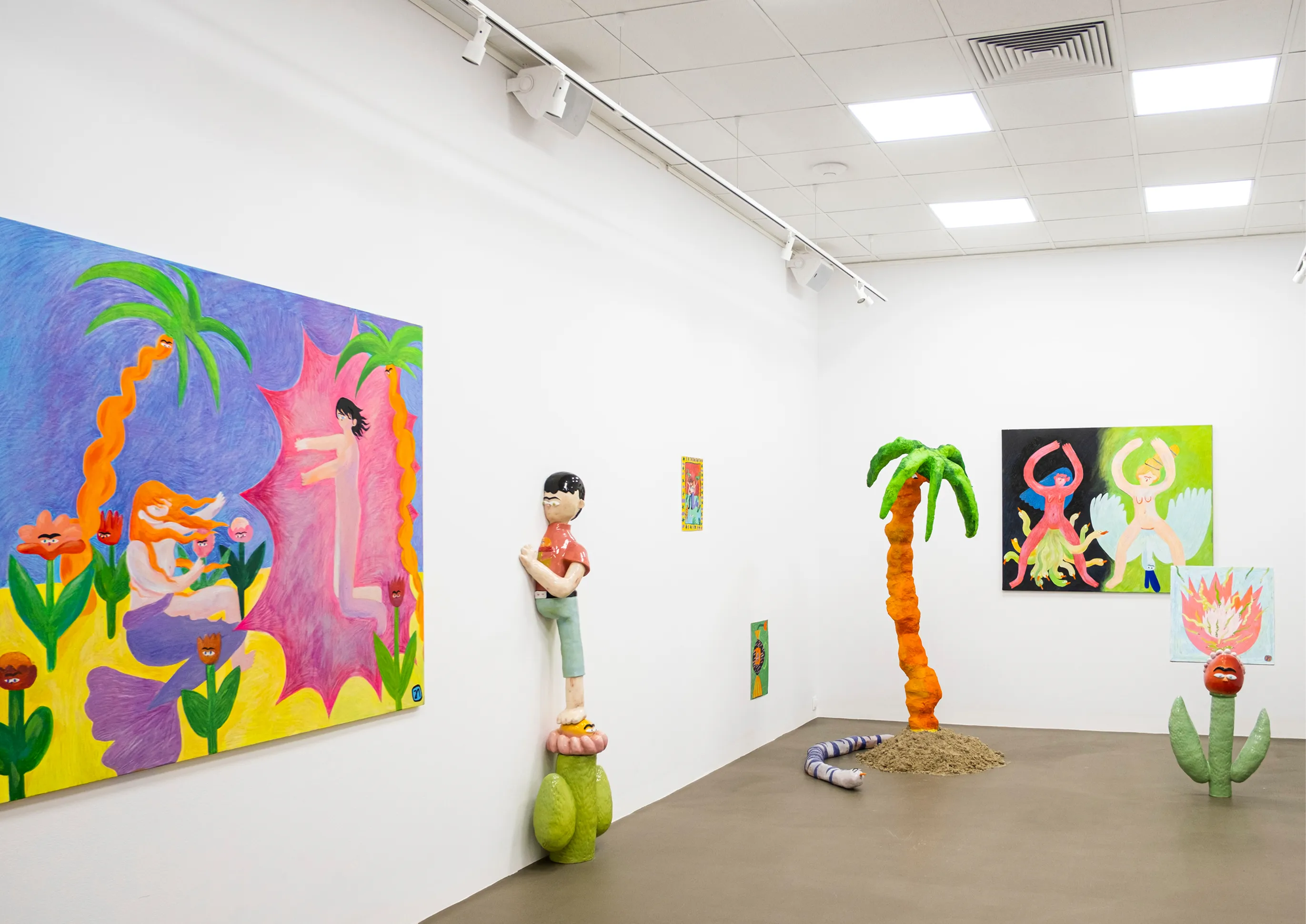 Wide gallery corner view with a large palm-tree painting, the boy-on-cactus figure, a sculptural palm tree, and a snake on the floor