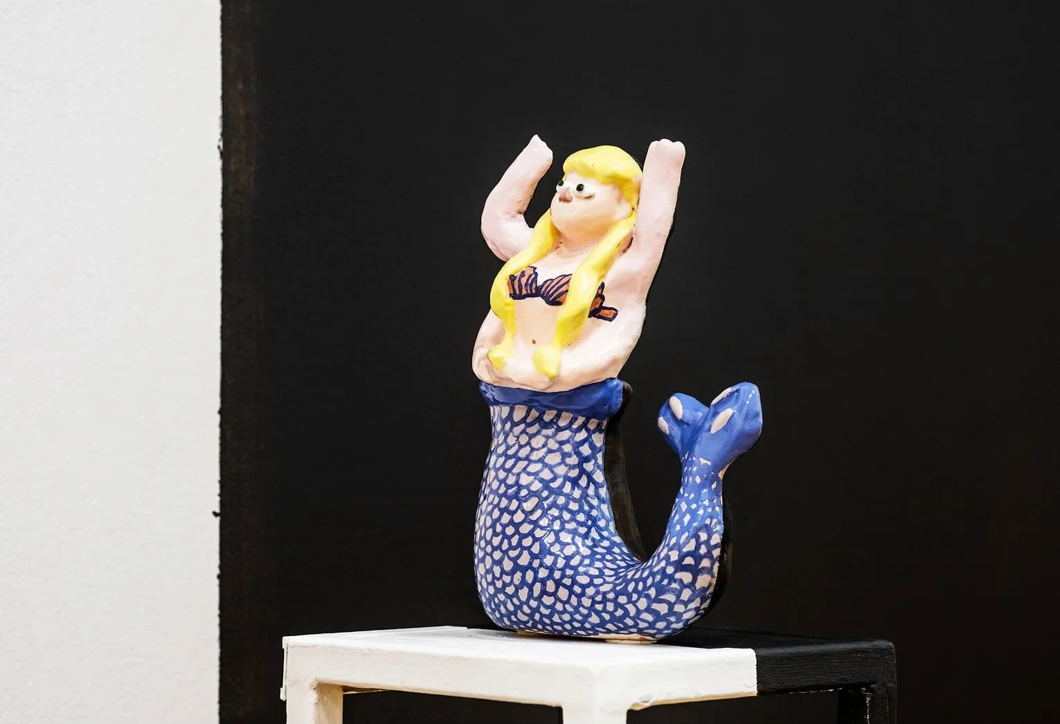 Ceramic figure of a mermaid with blonde hair and a blue scaled tail, arms raised overhead