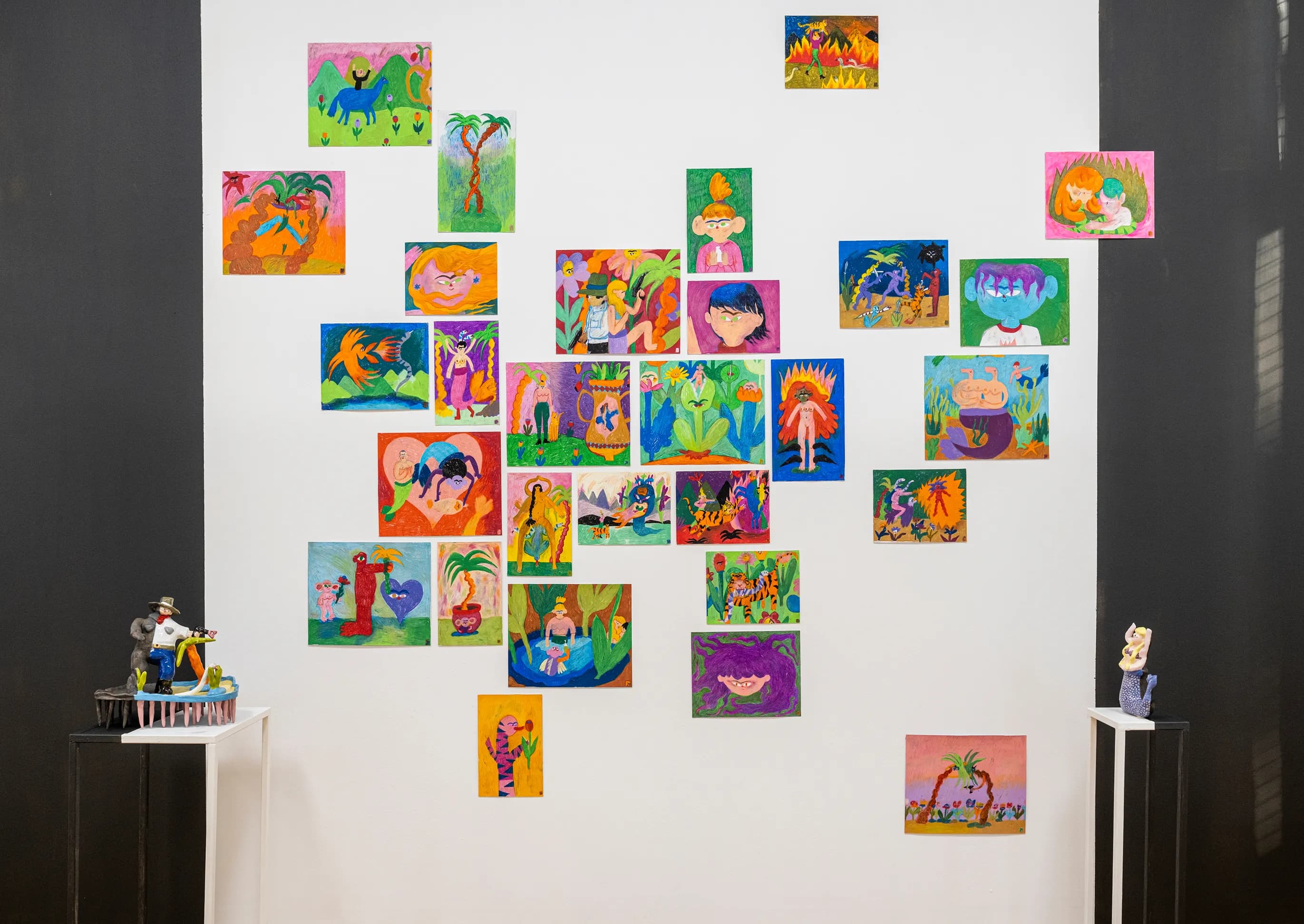 Salon-style wall hang of dozens of small colorful paintings, with sculptures on pedestals below