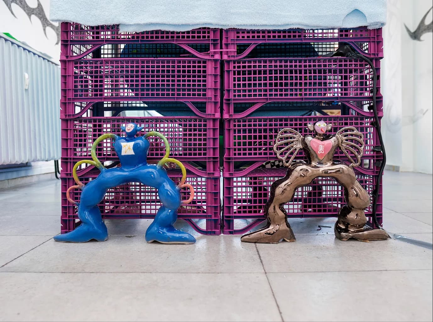 Detail of blue and bronze winged glazed figures standing beneath a crate table