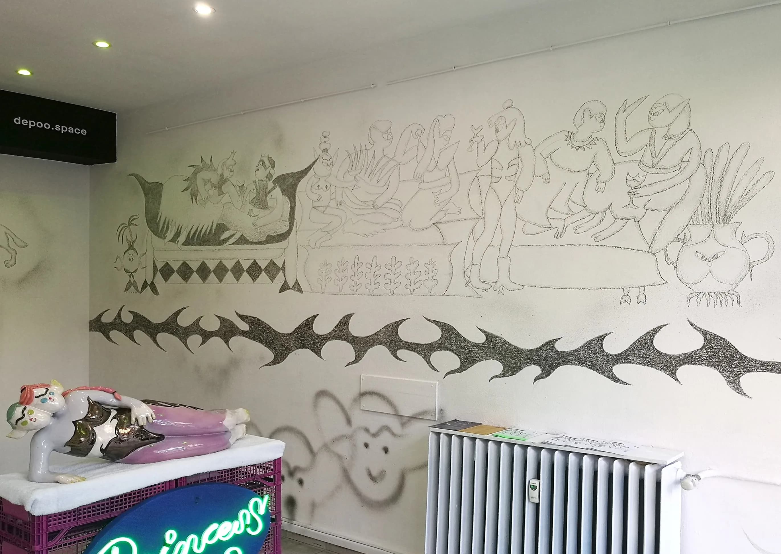 Wide installation view of a pencil mural of reclining banqueting figures with a thorn-vine motif and a pink glazed figure on crates