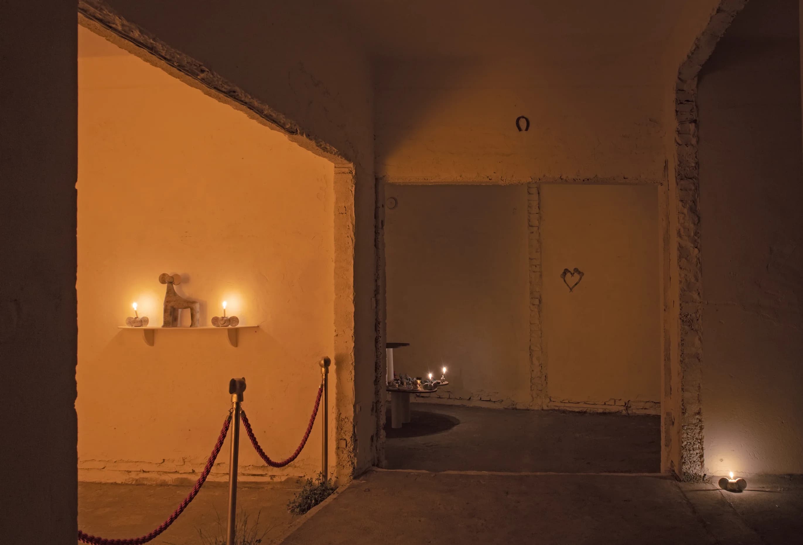 Dusk view through a doorway into candlelit rooms, with a velvet rope and a shelf of candles