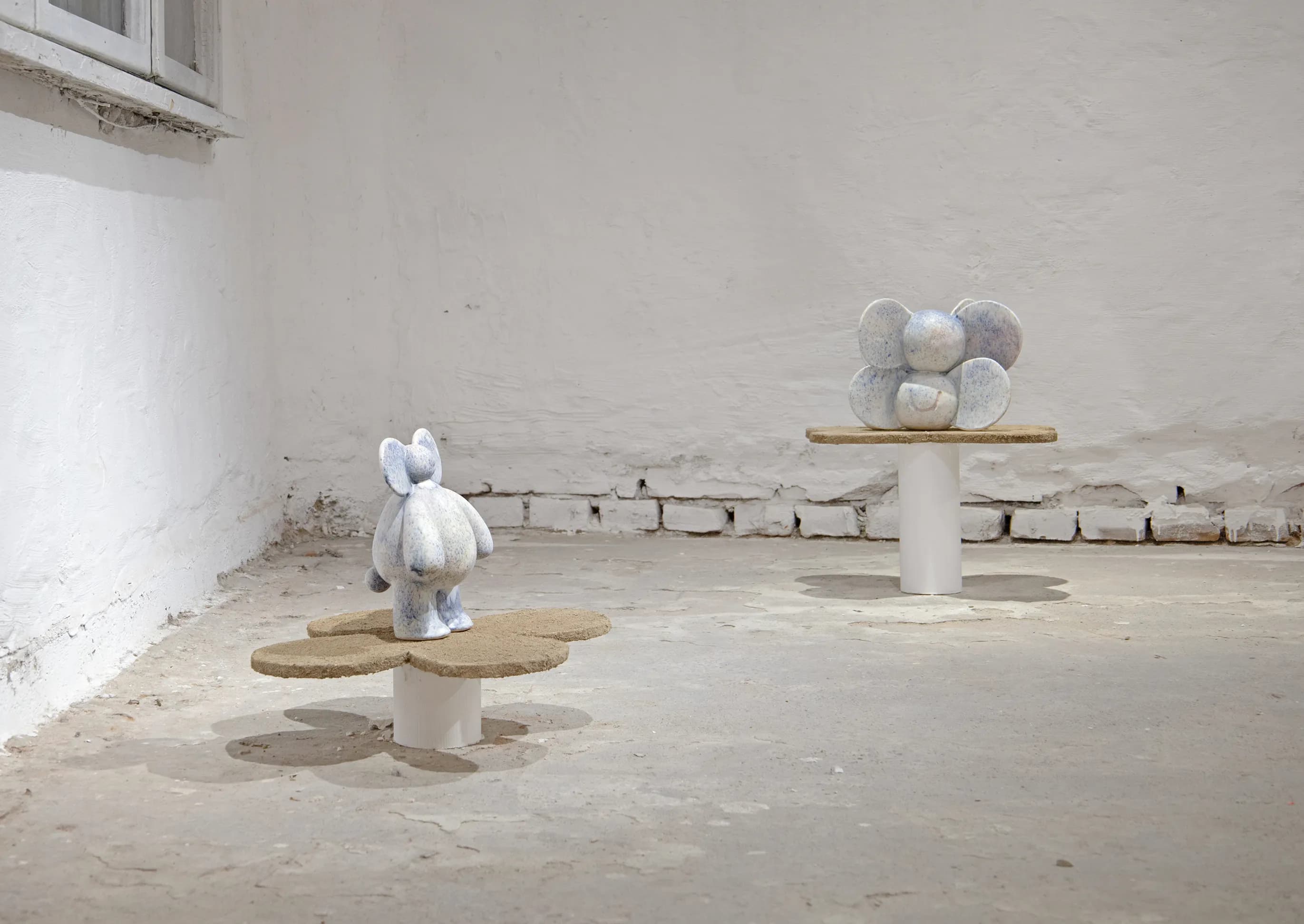 Two blue and white ceramic elephant-eared figures standing in an empty gallery room