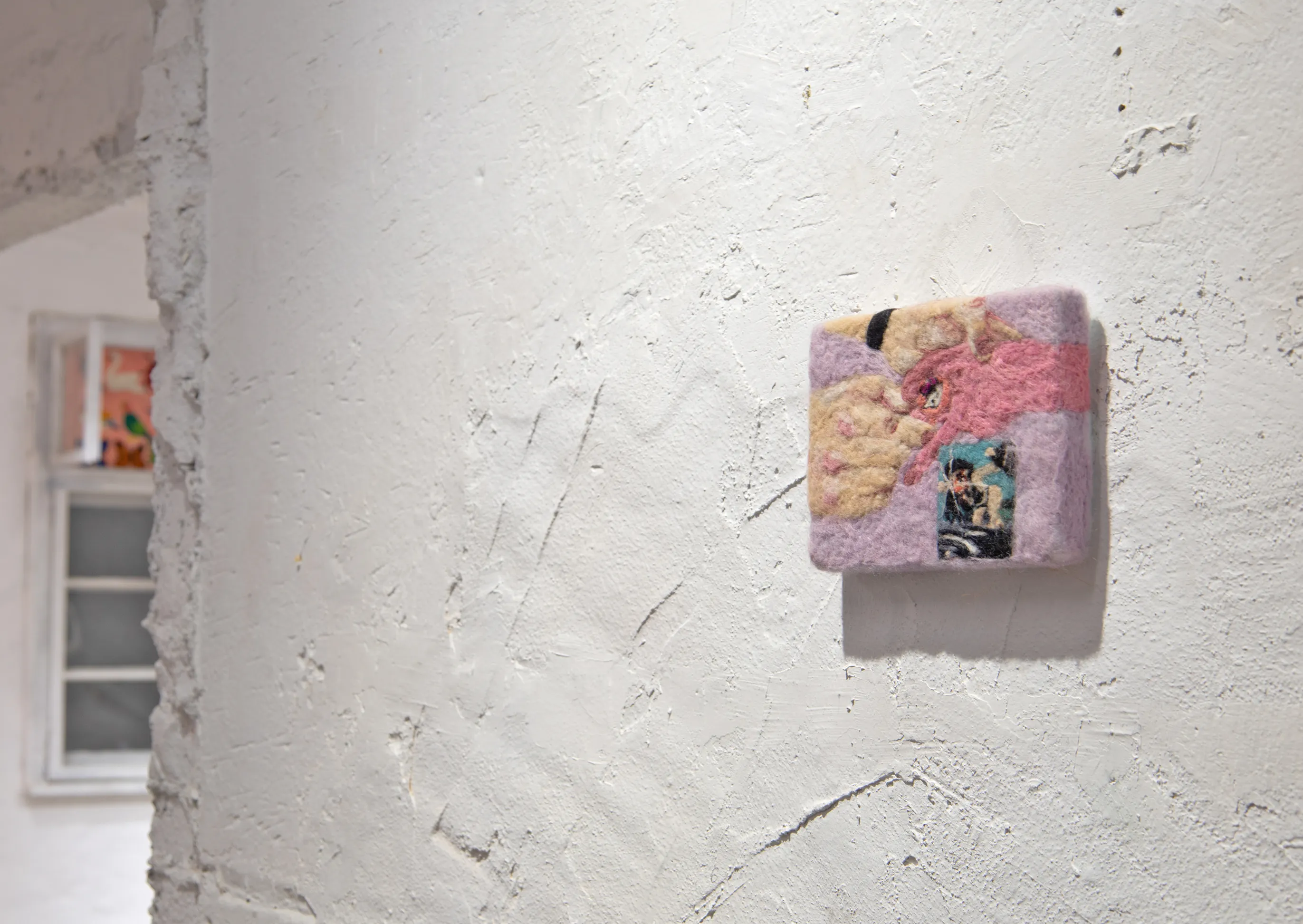 Detail of a small felted wall piece with embedded photographs, mounted on a rough plaster wall