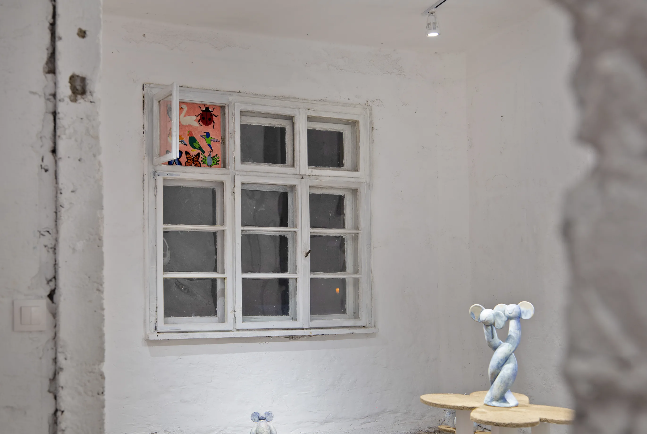 Gallery corner with a window and a decorated pane, and the twisted blue sculpture on the altar table