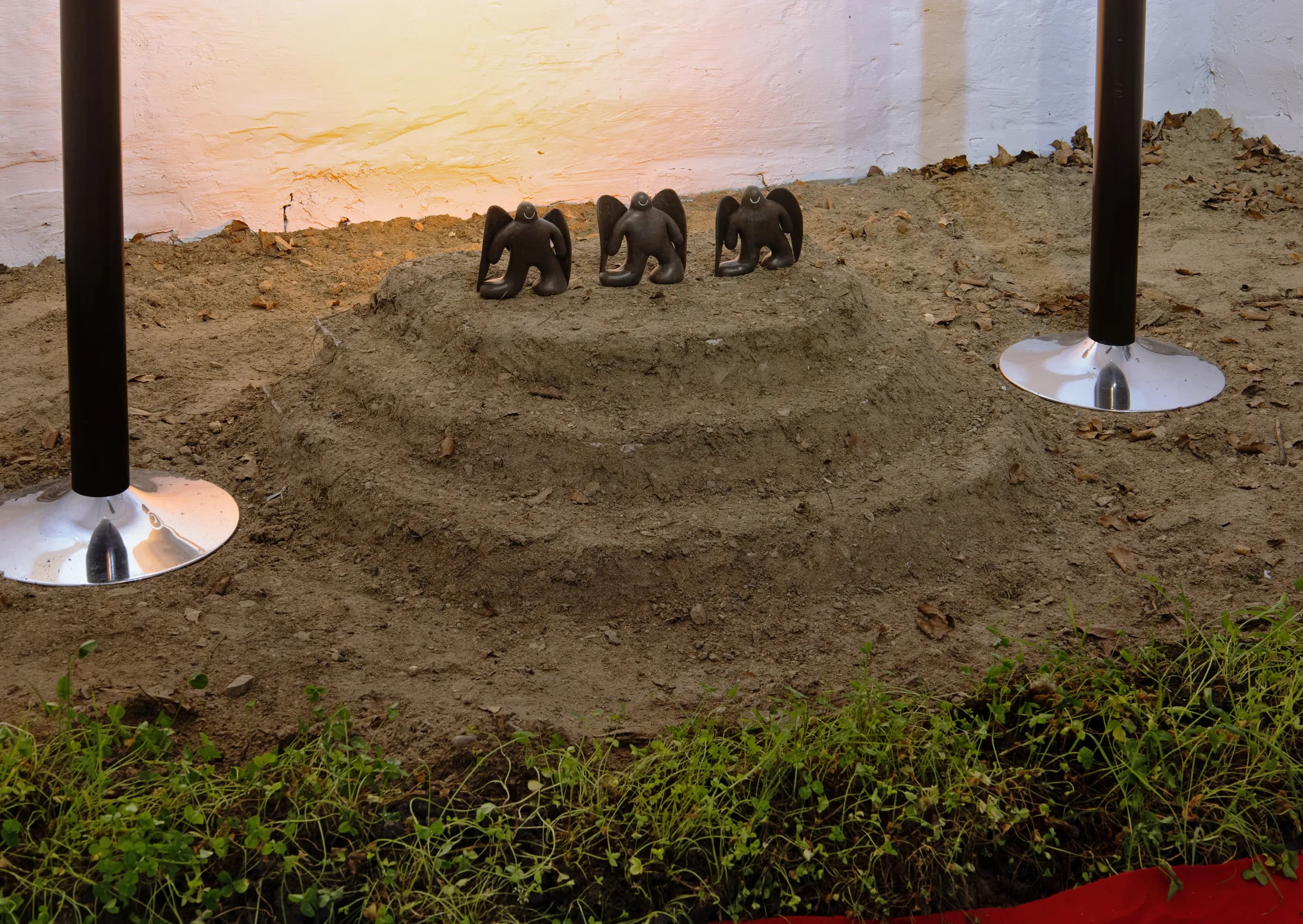 Detail of three small dark winged figurines kneeling on a sand mound between two rope-stand posts